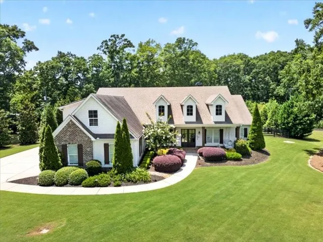 White siding exterior with brick accents, dormer windows, a covered entry, and extensive landscaping