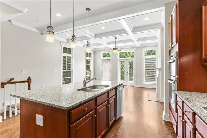 Kitchen with light stone countertops, dark wood-type flooring, beam ceiling, french doors, and coffered ceiling