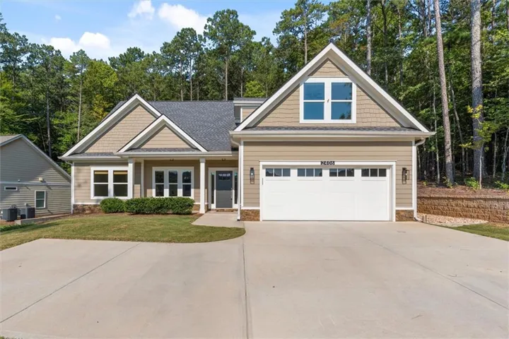 Two-car garage, neutral-toned siding, dark gray shingled roof, front porch, and mature trees