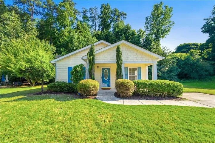 Charming cottage-style home featuring a cream-colored exterior with gabled roofline and blue accent door