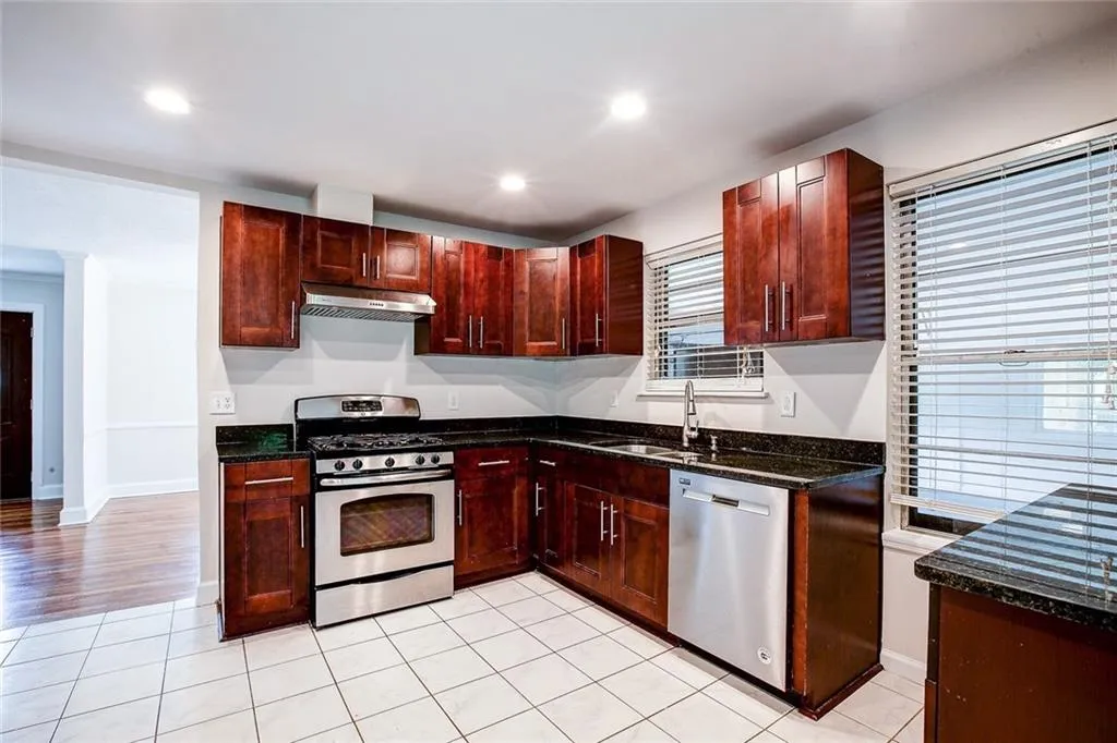 Kitchen with appliances with stainless steel finishes, sink, dark stone countertops, and light hardwood / wood-style flooring