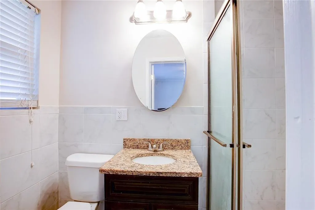 Bathroom featuring a shower with shower door, tile walls, toilet, and vanity