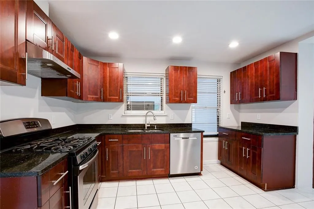 Kitchen featuring dark stone countertops, appliances with stainless steel finishes, sink, and light tile flooring