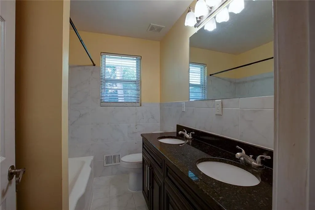 Full bathroom with tile floors, plenty of natural light, dual sinks, and tile walls