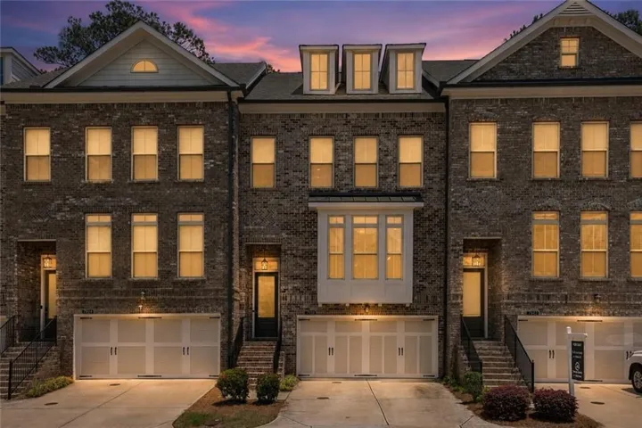 Brick facade townhome featuring multiple windows, a two-car garage, and a covered entry