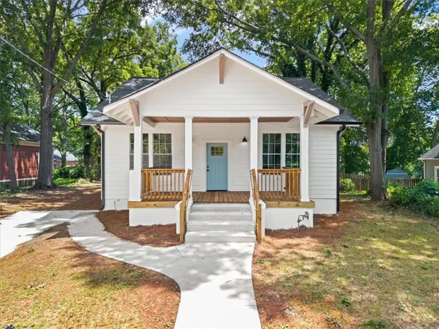 White clapboard siding, covered front porch with wood railings, light blue front door, concrete walkway, and dark shingle roof