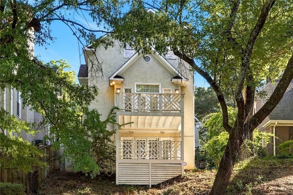 Stucco exterior featuring a two-story deck with geometric lattice railings, gabled roofline, and glass-paned doors