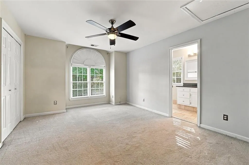 Room featuring wall-to-wall carpeting, a multi-pane window with an arched transom, a central ceiling fan with integrated lighting, and dual-panel closet doors