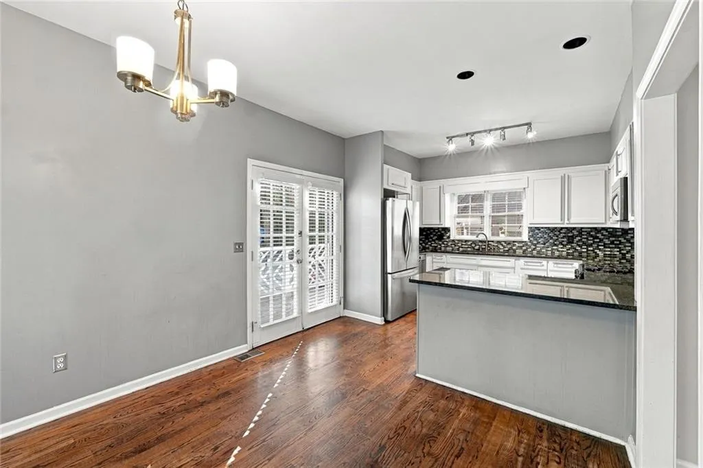 Kitchen featuring white cabinetry, stone countertops, stainless steel appliances, wood-finish flooring, and a multi-arm chandelier