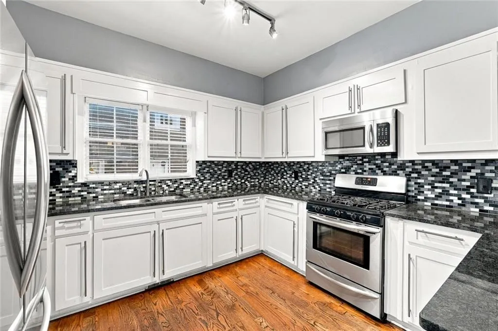 Kitchen featuring white cabinetry, stone countertops, multi-tonal mosaic tile backsplash, stainless steel appliances, and wood-finish flooring
