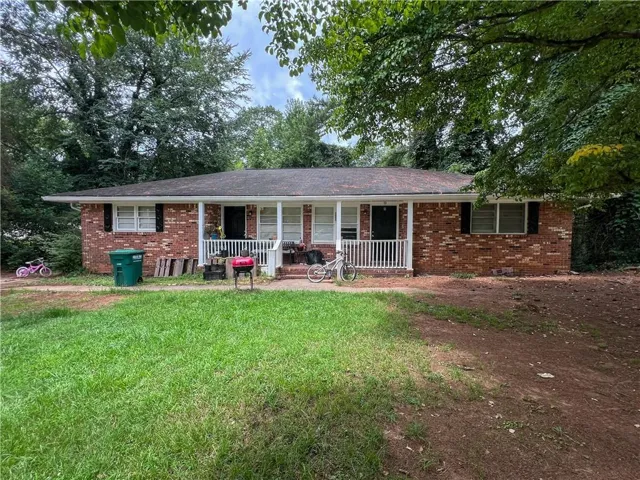 Brick exterior featuring a covered front porch with white railing, black window shutters, and a shingle roof