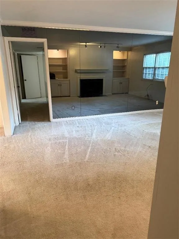 Unfurnished living room with carpet floors, a fireplace, and crown molding