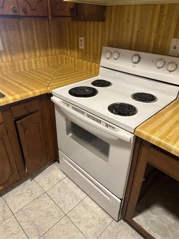Kitchen with light countertops, white electric range, dark brown cabinets, and light tile patterned flooring