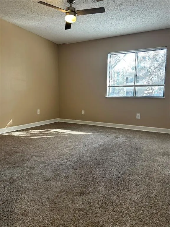 Unfurnished room with dark carpet, a ceiling fan, and a textured ceiling