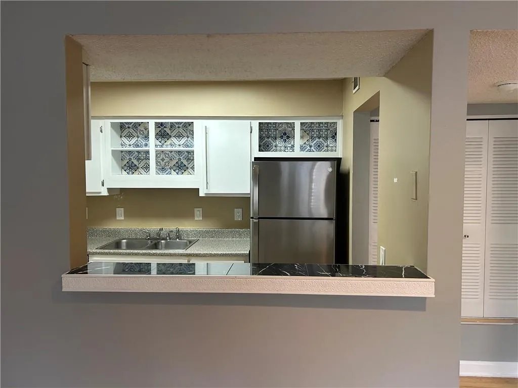 Kitchen featuring freestanding refrigerator, white cabinets, a textured ceiling, and light countertops