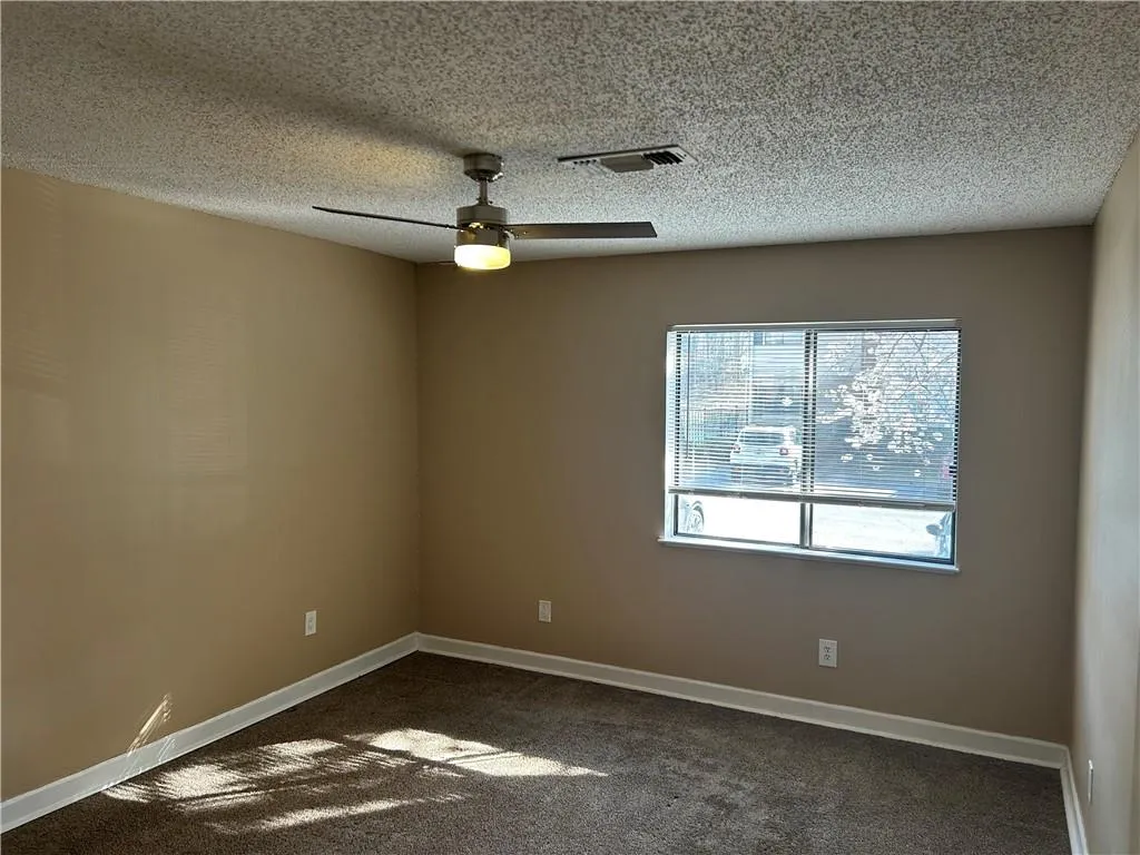 Unfurnished room featuring a ceiling fan, dark carpet, and a textured ceiling