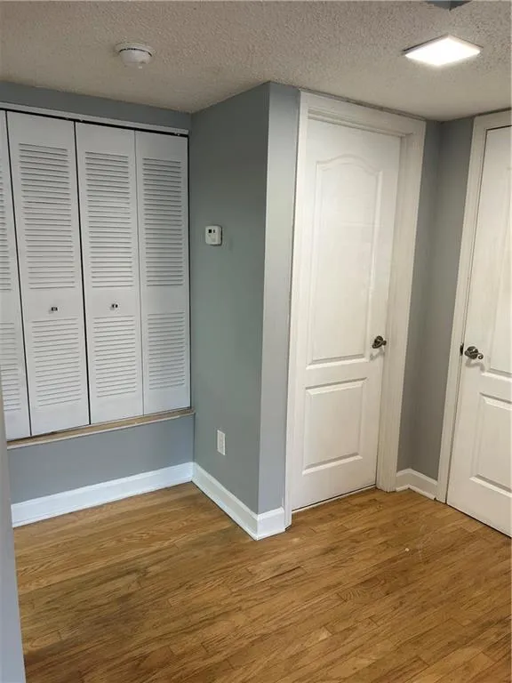 Unfurnished bedroom featuring a textured ceiling, wood finished floors, and a closet