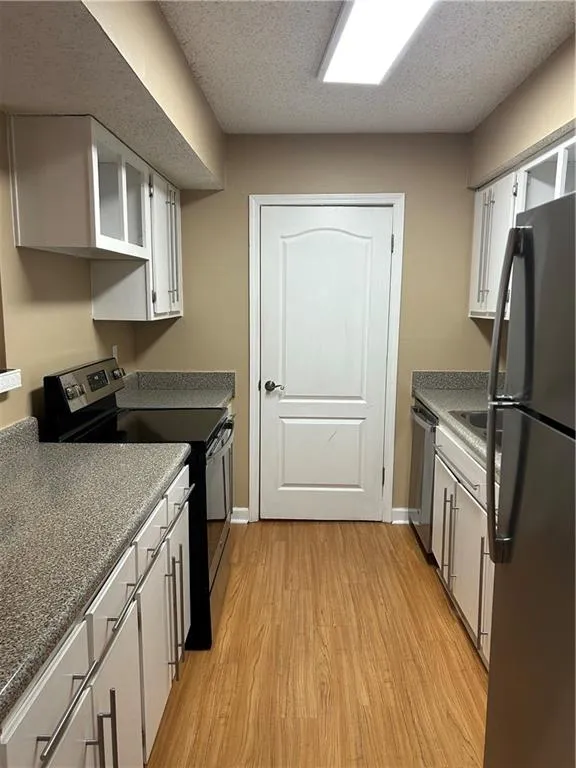 Kitchen featuring range, white cabinets, fridge, light wood-type flooring, and a textured ceiling