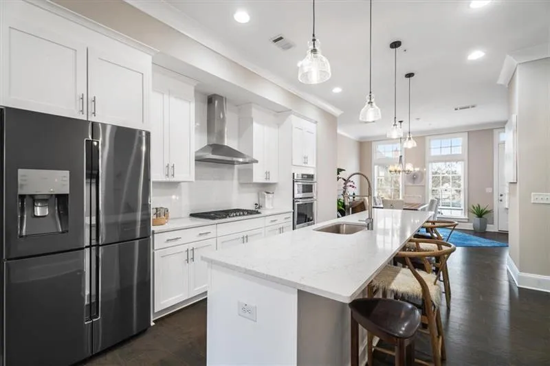Kitchen with appliances with stainless steel finishes, hanging light fixtures, wall chimney exhaust hood, and a kitchen island with sink