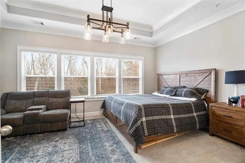 Carpeted bedroom with a notable chandelier, ornamental molding, and a raised ceiling