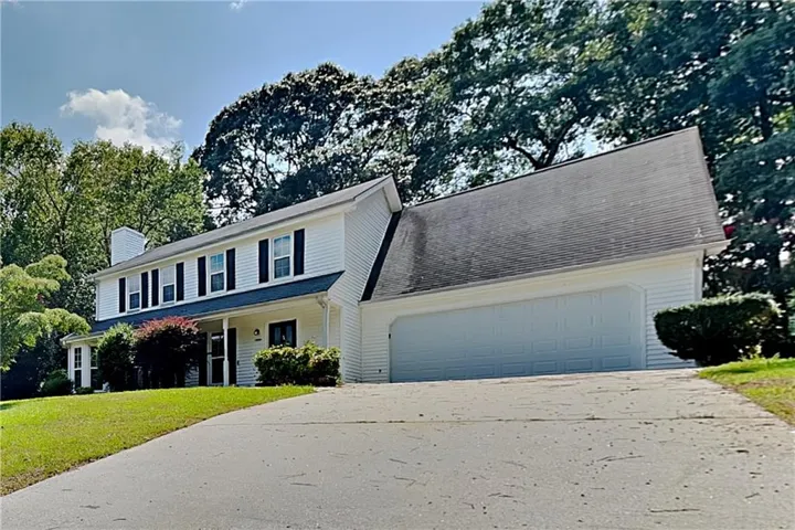 Two-story exterior with white siding, black shutters, covered front porch, attached garage, and a concrete driveway