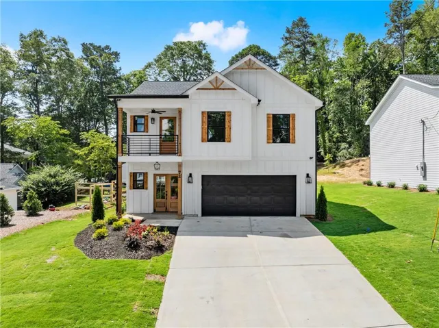 Modern farmhouse exterior featuring white board and batten siding, dark framed windows with wood shutters, an attached two-car garage with a dark door, a concrete driveway, and a second-story balcony with a black metal railing