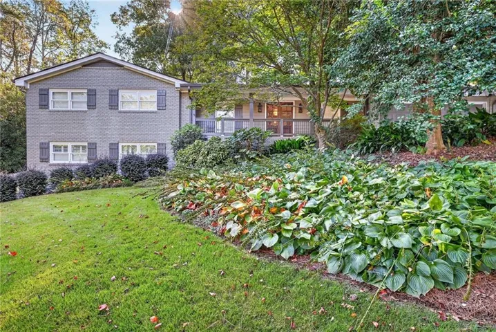 Brick exterior with gray shutters, front lawn with mature landscaping, and an elevated porch with wood railing