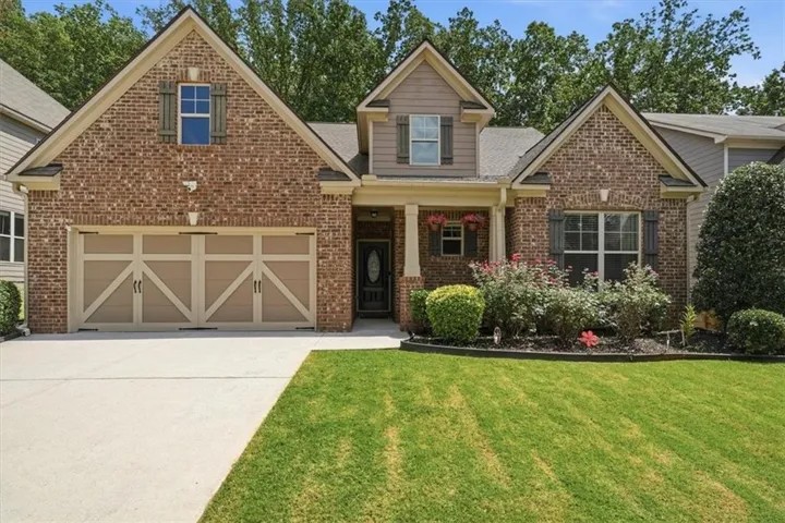 Brick and siding exterior, two-car garage with carriage-style doors, front porch with columns, landscaped front yard, and concrete driveway
