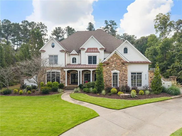 Stately residence featuring a white stucco and stone exterior, a covered entryway, multiple gables, and a concrete driveway
