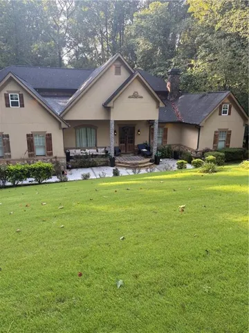 Stucco exterior with wood shutters, stone-clad columns, double-door entry, and a stone chimney