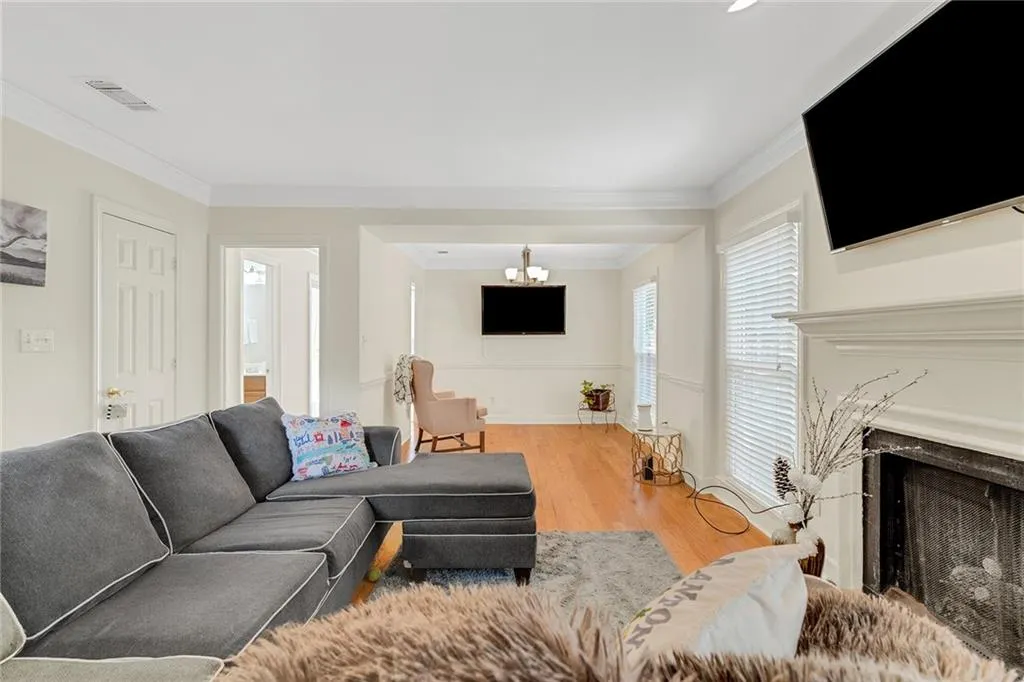 Living room featuring wood-type flooring, a notable chandelier, crown molding, and a high end fireplace