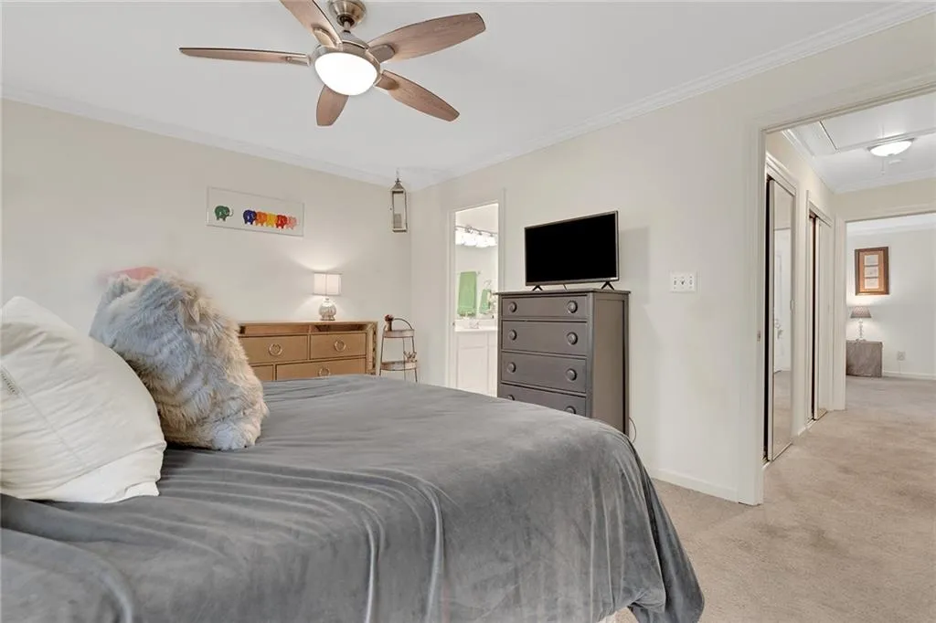 Bedroom with ensuite bath, ceiling fan, ornamental molding, and light colored carpet