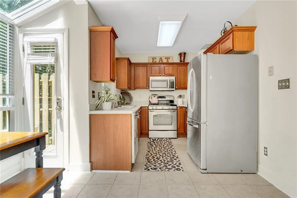 Kitchen with appliances with stainless steel finishes, lofted ceiling with skylight, light tile patterned floors, and sink
