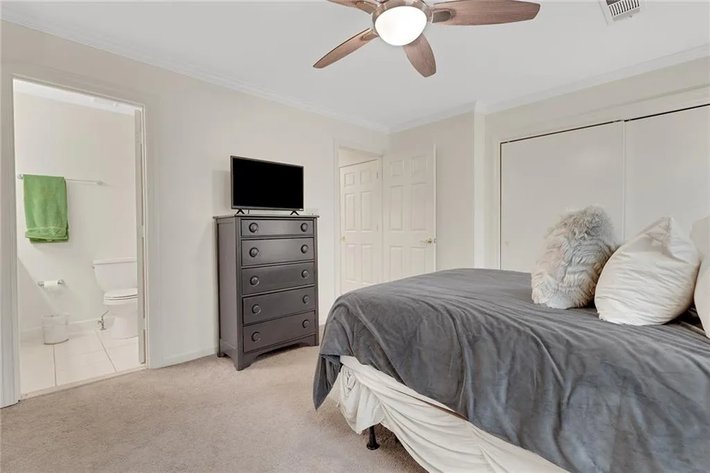 Carpeted bedroom featuring ornamental molding, ensuite bathroom, and ceiling fan