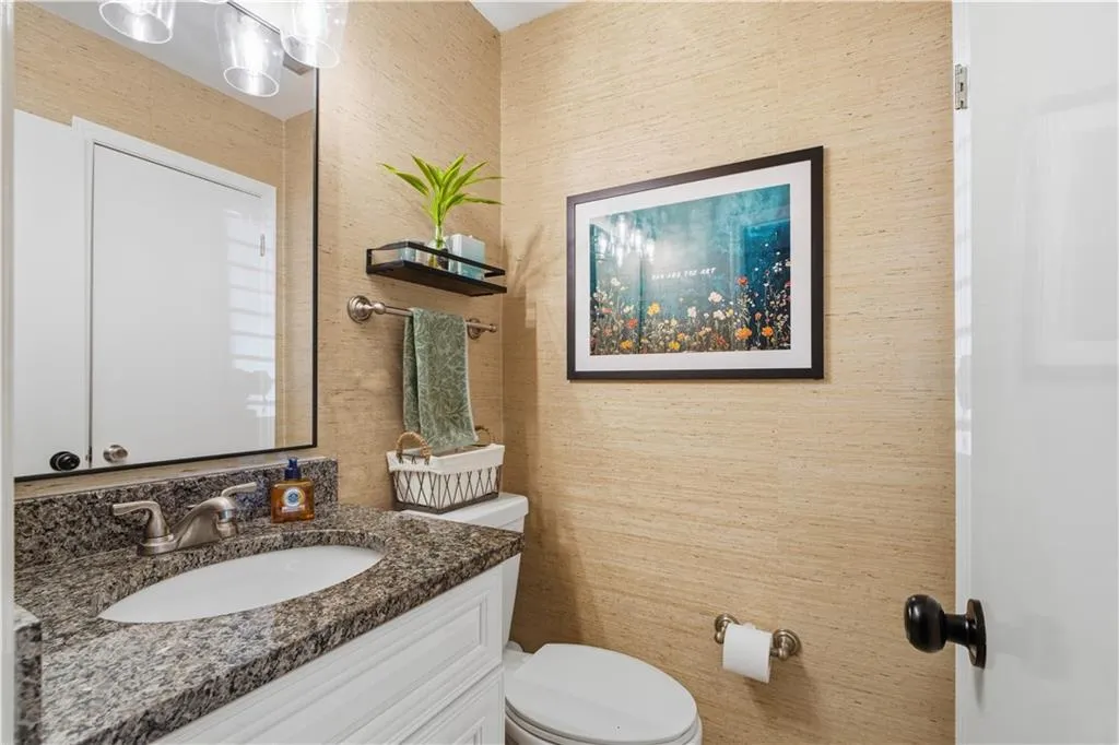 Granite countertop with an undermount sink, white vanity cabinetry, wall-mounted mirror, and a modern light fixture