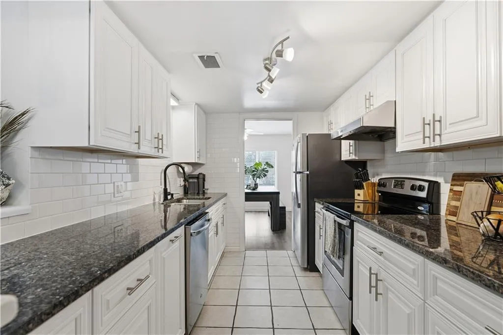 Galley kitchen featuring white cabinetry, dark stone countertops, stainless steel appliances, a white subway tile backsplash, and track lighting