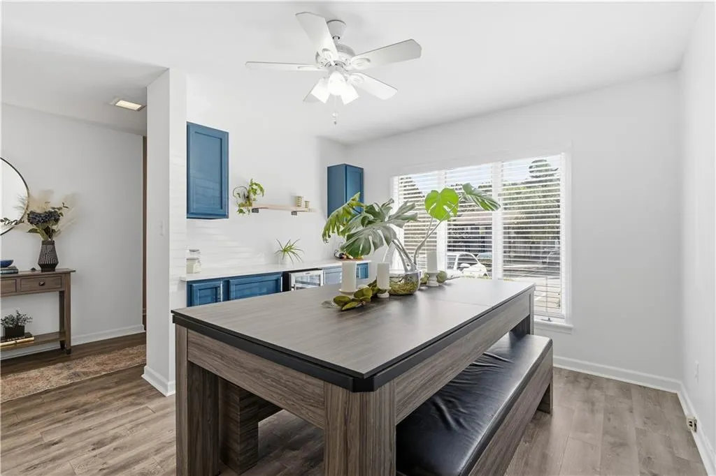 Wood-finish flooring throughout, bright white walls, white ceiling fan, and a built-in wet bar with blue cabinetry