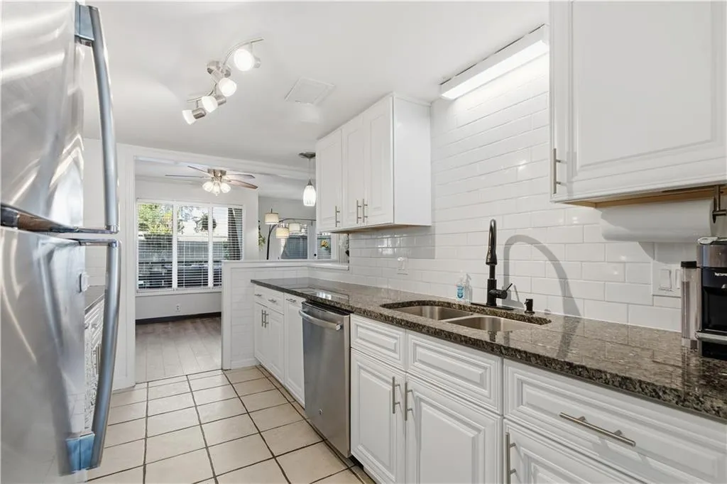 White shaker cabinetry, dark speckled countertops, stainless steel appliances, white subway tile backsplash, and a dual basin sink with a matte black faucet