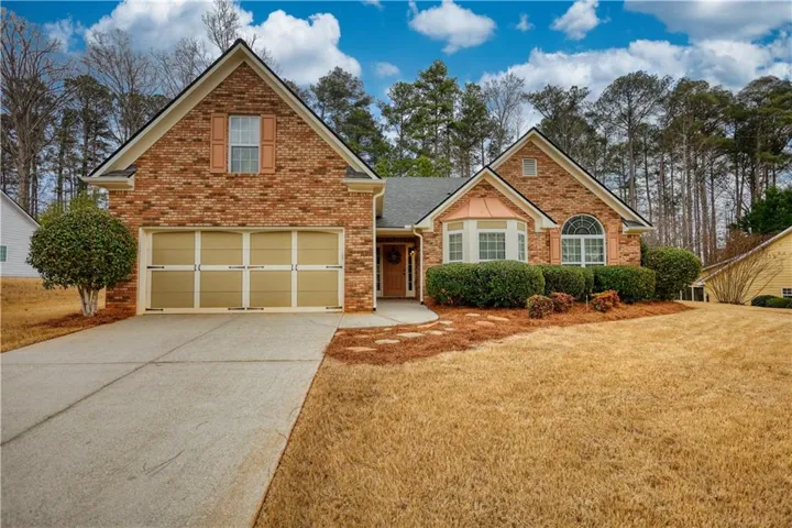 Traditional home featuring brick siding, driveway, a garage, and a front lawn