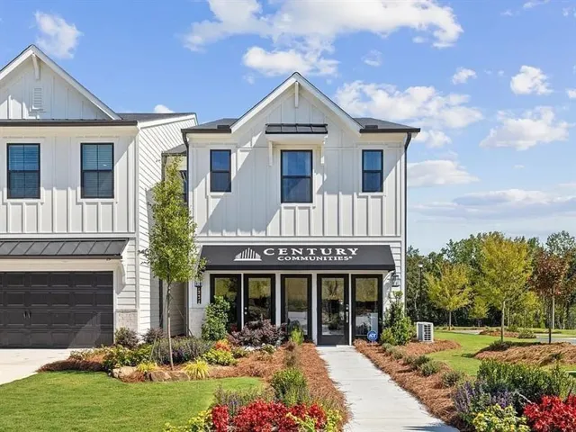 Modern farmhouse-style exterior featuring vertical white siding, black-framed windows, a prominent black awning, and a concrete pathway bordered by landscaped garden beds
