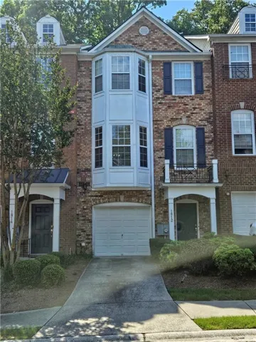 Brick townhouse exterior featuring a prominent bay window, attached garage, dormer windows, and a covered front entry