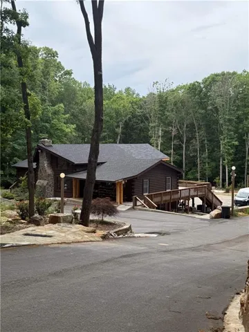 Log cabin exterior featuring a stone chimney, a dark shingle roof, and a wood deck with stairs and a ramp