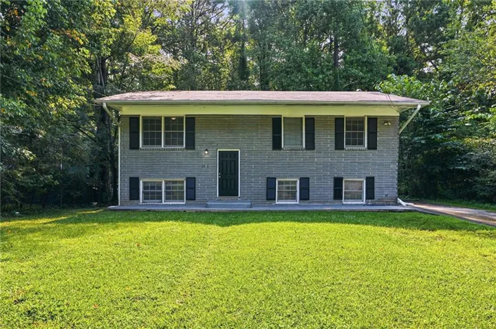 Gray brick exterior with black shutters, mature tree surroundings, and an expansive front lawn