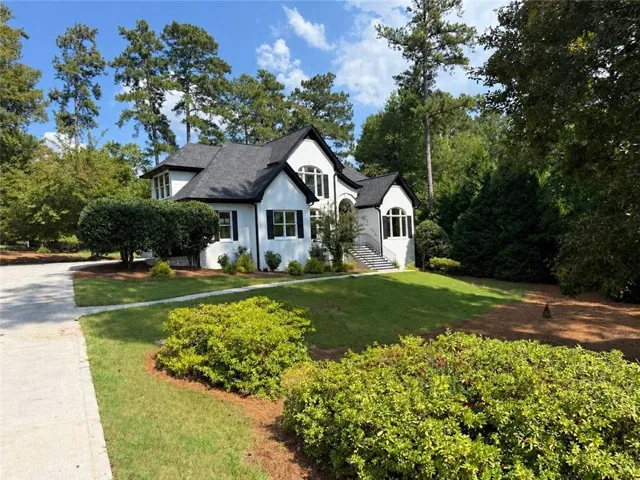 White exterior with black accents, gabled roofline, multiple windows with dark shutters, established landscaping, and a concrete driveway