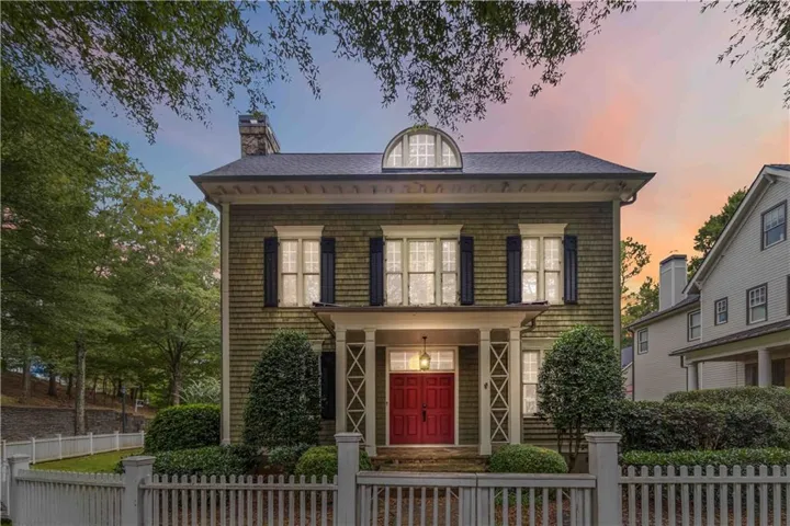 Georgian-style home with a porch, a chimney, and a fenced front yard