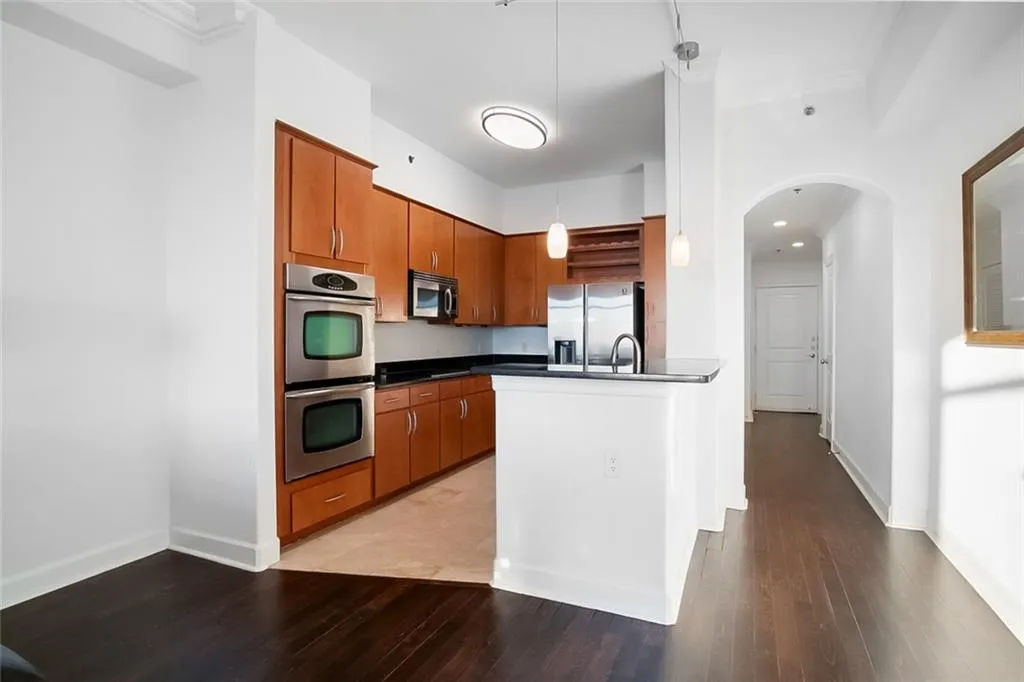 Kitchen featuring light wood finished floors, dark countertops, brown cabinetry, and appliances with stainless steel finishes