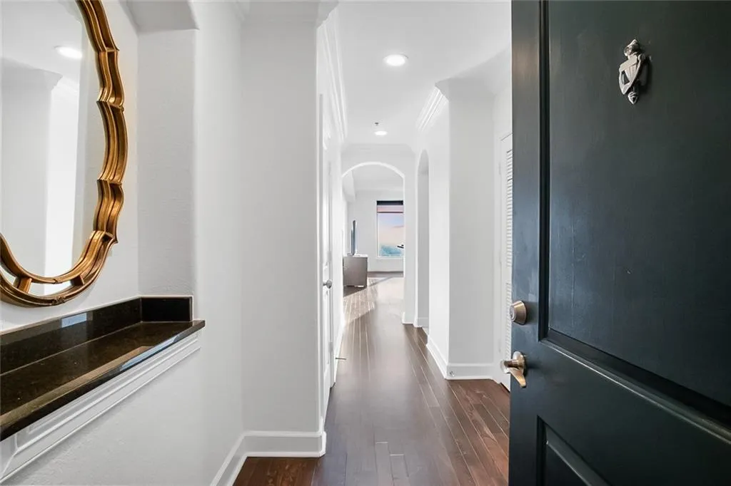 Hall with ornamental molding, dark wood-style flooring, arched walkways, and baseboards