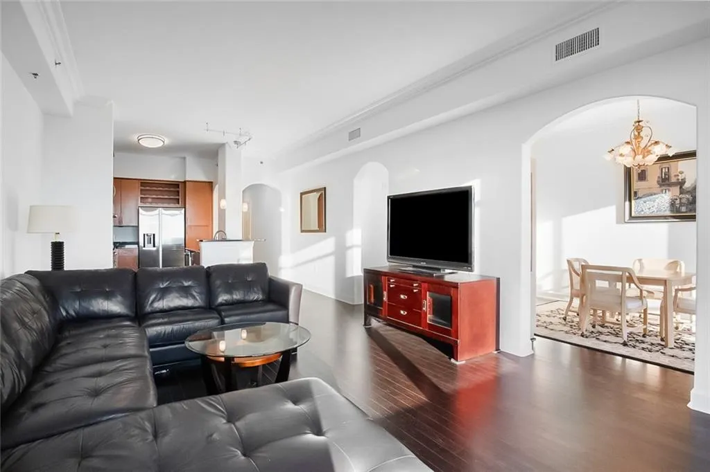 Living area with dark wood-style flooring, visible vents, crown molding, arched walkways, and a notable chandelier