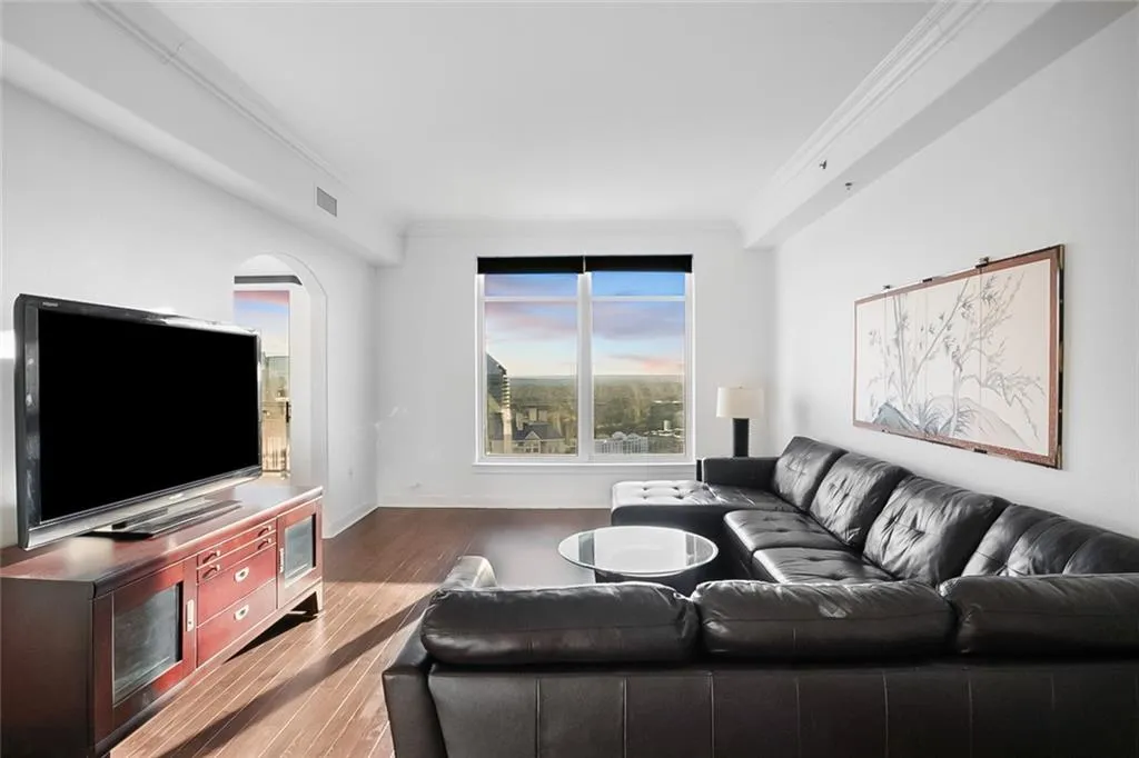 Living room featuring wood finished floors, baseboards, visible vents, arched walkways, and ornamental molding