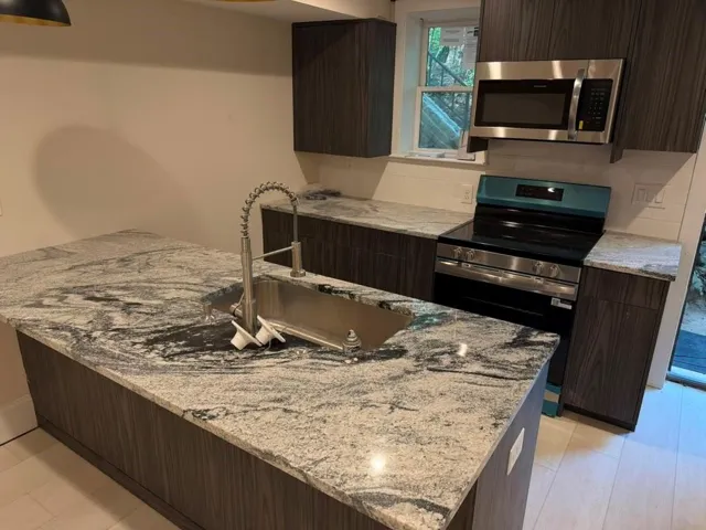 Kitchen with wood-finish cabinetry, patterned countertops, stainless steel appliances, and a tile backsplash